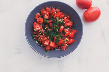 Tomates cortados em pedaços pequenos, com temperos verdes por cima. A salada está numa tijela cinza.