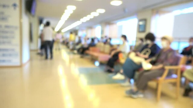 Blurred shot of patients with mask waiting in the crowded lobby at hospital in Japan. Social distancing. 4K
