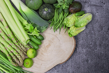 Green vegetables of different varieties lie in a semicircle on a wooden frame on the left and with space for text on the right, close-up top view.