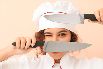 Female African-American chef with knives on color background