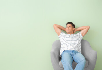 Young man relaxing in armchair near color wall