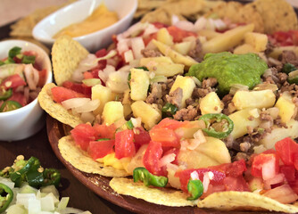 Side view of delicious nachos with cheese, chopped tomato, chips, jalapeno chili and green sauce. Spending time with friends with delicious food.