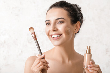 Beautiful young woman with foundation on her face against light background