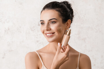 Beautiful young woman with foundation on her face against light background