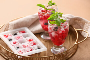 Glasses with ice and frozen berries on color background