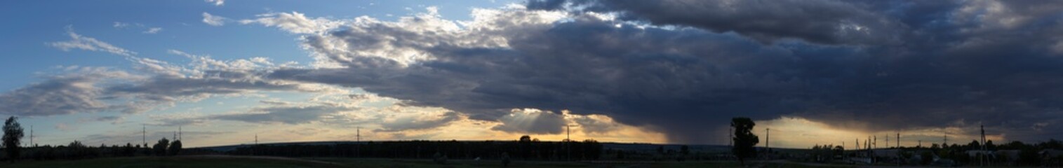 Landscape at sunset. A thunderstorm is approaching the village. Tragic gloomy sky. Panorama.