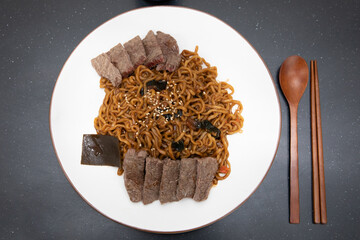 Top view image of Korean black bean noodles, Jajjangmyeon with wooden spoon and chopstick.
