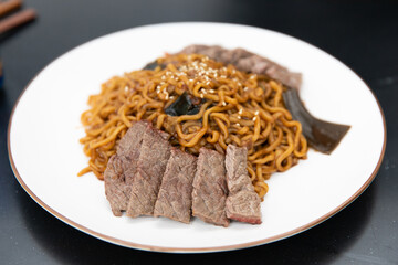 Korean black bean sauce noodles with saliced meat on a plate.
