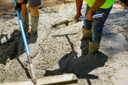 Mason building a screed coat cement a laborer floats a new concrete sidewalk