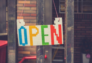 An "Open" sign hanging on a metal door. Toned image.