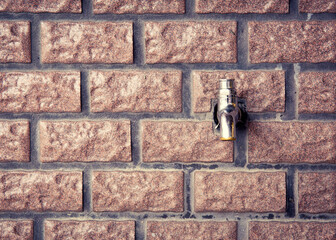 A faucet on a red brick wall. Toned image.