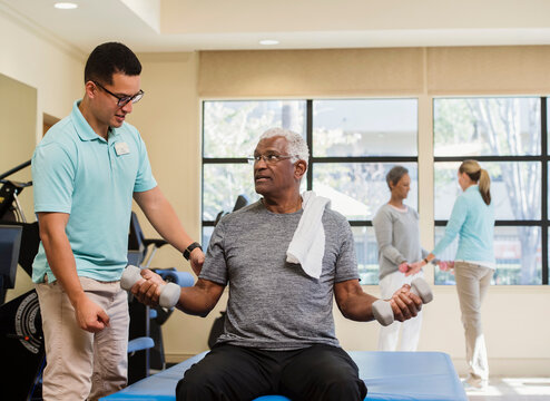  Senior Couple Exercising With Trainer In Gym