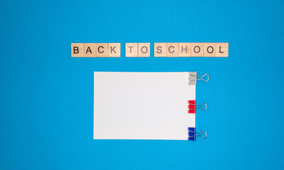 On a blue background, a notebook sheet and a phrase made of wooden letters, back to school, the concept of returning to school after the holidays.