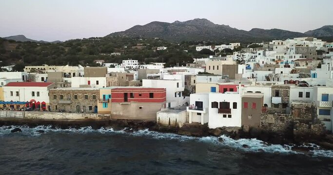 Panorama shot of the small greek village on the shore, sea and waves hitting quay