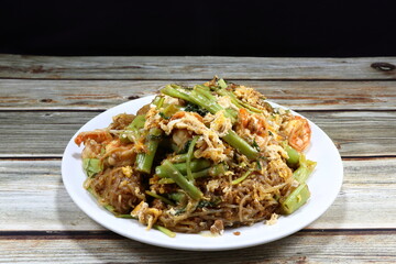 Traditional fried rice noodle with peeled shrimp, cutting fresh morning glory and bean sprouts on the plate. Famous Thai style stirred noodle with fish sauce and pepper. 