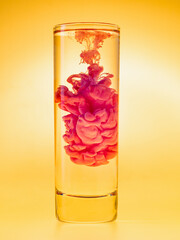 Red ink cloud in glass of water. Studio shot. Paint in water on yellow background. Analog color scheme