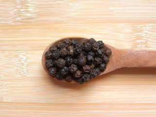 Black color raw whole dried pepper on wooden spoon