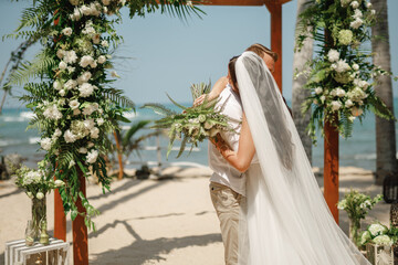 Bride and groom enjoying beach wedding in tropics, wedding arch, ocean background