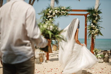 Bride and groom enjoying beach wedding in tropics, wedding arch, ocean background