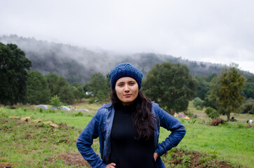 mujer en la montaña con neblina por la mañana con las manos en la cintura y zona de camping