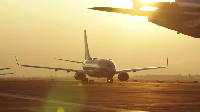 One airplane waits on the runway for takeof. The foreground airplane moves away and reveals a lens flare. camera is locked