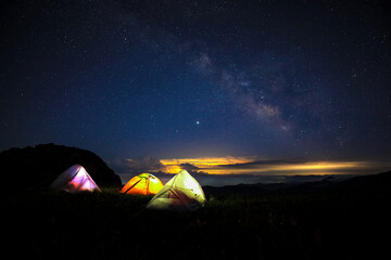 Three tents under the beautiful starry sky glowed in the middle of the night. The orange tent under the Milky way at night.