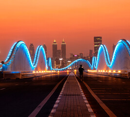 Illuminated Meydan bridge and view of Dubai city at dusk