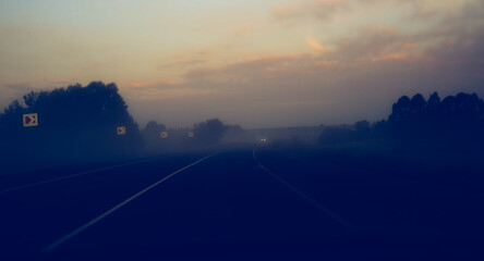 Car road at dawn with a view of fog and lights from an oncoming car