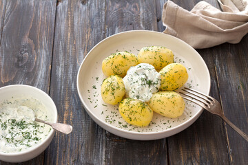 Young boiled potatoes with dill and garlic sour cream sauce on wooden table