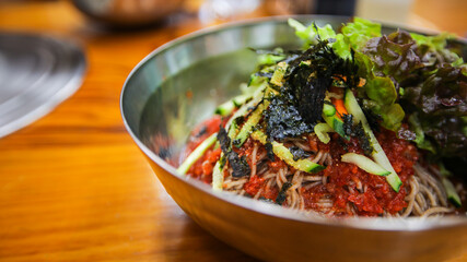 Korean traditional food, spicy cold soba noodles, Bibim Guksu, with lettuce and vegetables on a stainless steel bowl