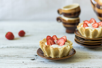 Dessert tartlets with butter cream and fresh strawberries on a white wooden background. Ceramic tableware for saina or coffee ceremony. Horizontal orientation