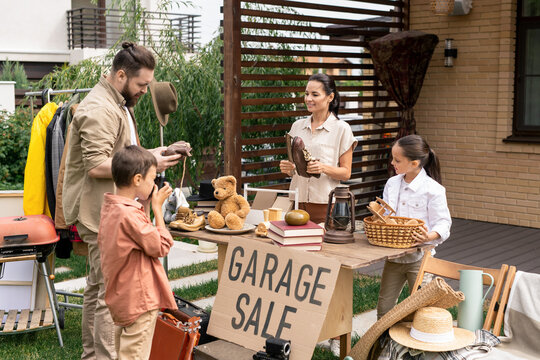 Bearded Man Choosing Goods At Garage Sale While His Son Photographing Girl At Table