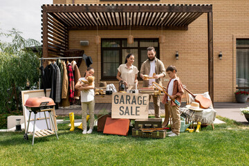 Young family standing against brick house and saying goodbye to old things at garage sale