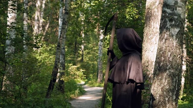 Death Grim Reaper with Scythe Walking in a Park. Slow Motion. Life and Death, Another World and Halloween Concept