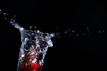 Strawberries fall into a glass of water. Water spills out of a glass.Making drinks. Carbonated drinks. Fruit drinks. Making a cocktail. Refreshing drinks. .Mix drinks. Water splashes.Splashing water.