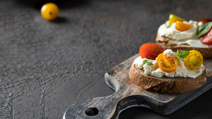 Homemade bruschetta on wooden cut board ,grilled bread slices with cream cheese and different tomato cherry  garnished with fresh basil leaves. Delicious starter