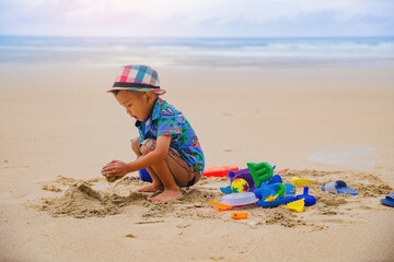 Asian boy playing with sand toys at tropical beach in holiday. Family summer vacation.