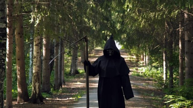 Scary Skeleton Grim Reaper with Scythe in Hand Walking in a Park. Slow Motion. Life and Death, Another World and Halloween Concept