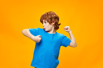 Happy red-haired boy in a blue T-shirt on a yellow background dances - obrazy, fototapety, plakaty