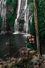 Fototapeta premium Lovers at the waterfall. Beautiful couple at a waterfall in Indonesia. A couple in love travels around the island of Bali. A man and a woman kiss at the waterfall. Travel to Asia. Сopy space