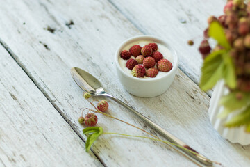 Ripe and green strawberries with leaves and flowers in a ceramic vase on a white background. Dessert with cream and berries in a white bowl. Light snack