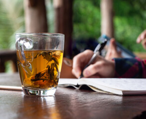 Flower tea cup on wooden table in  lush green background, hand writing on notebook.