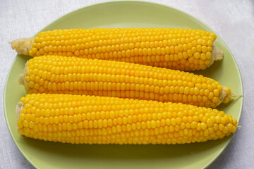 Yellow boiled corn on a green plate. Three ears of boiled corn.