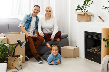 Fototapeta na wymiar Happy family sitting on wooden floor. Father, mother and child having fun together. Moving house day, new home and design interior concept