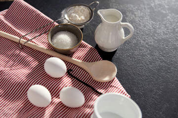 cooking food, culinary and recipe concept - eggs, milk, flour, wooden spoon and vanilla extract on table