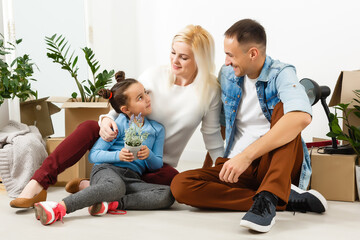 Happy family sitting on wooden floor. Father, mother and child having fun together. Moving house day, new home and design interior concept