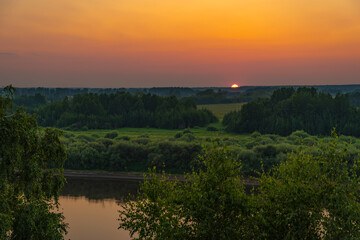Fototapeta na wymiar Beautiful views of the sunset over the river with trees, fields and flowers