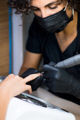 manicurist master in black gloves and mask is making manicure with a manicure drill apparatus