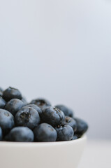 Macro of freshly picked blueberry with water drops in white bowl on blue background. Sweet ripe berries close up 