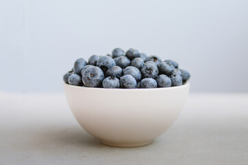 Minimalistic photo of freshly picked blueberry in white bowl on dark blue background. Handful of sweet ripe berries close up 